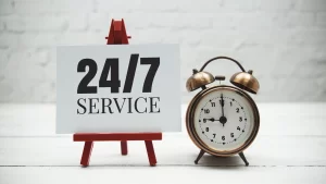 An alarm clock beside a 24/7 service sign symbolizing fast emergency portable toilet rentals during urgent response