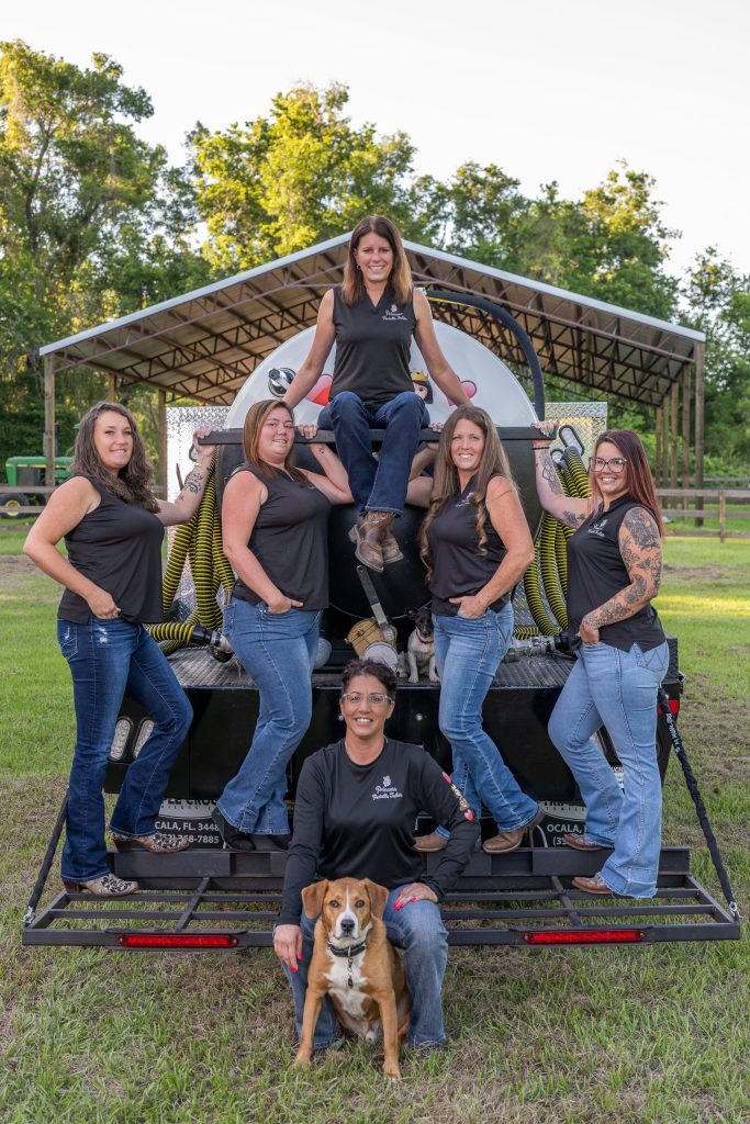 Professional all-women team from Princess Portable Toilets posing confidently with their service truck and equipment, showcasing strength, teamwork, and reliable sanitation services in a rural outdoor setting.